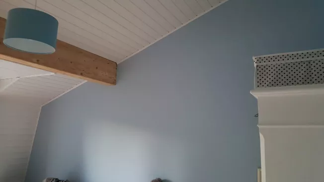Chambre repeinte en bleu-gris sous un plafond lambrissé blanc, prête à être relouée