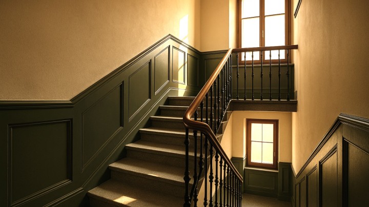 Cage d'escalier d'immeuble ancien rénovée, boiseries vert foncé et rampe en fer forgé