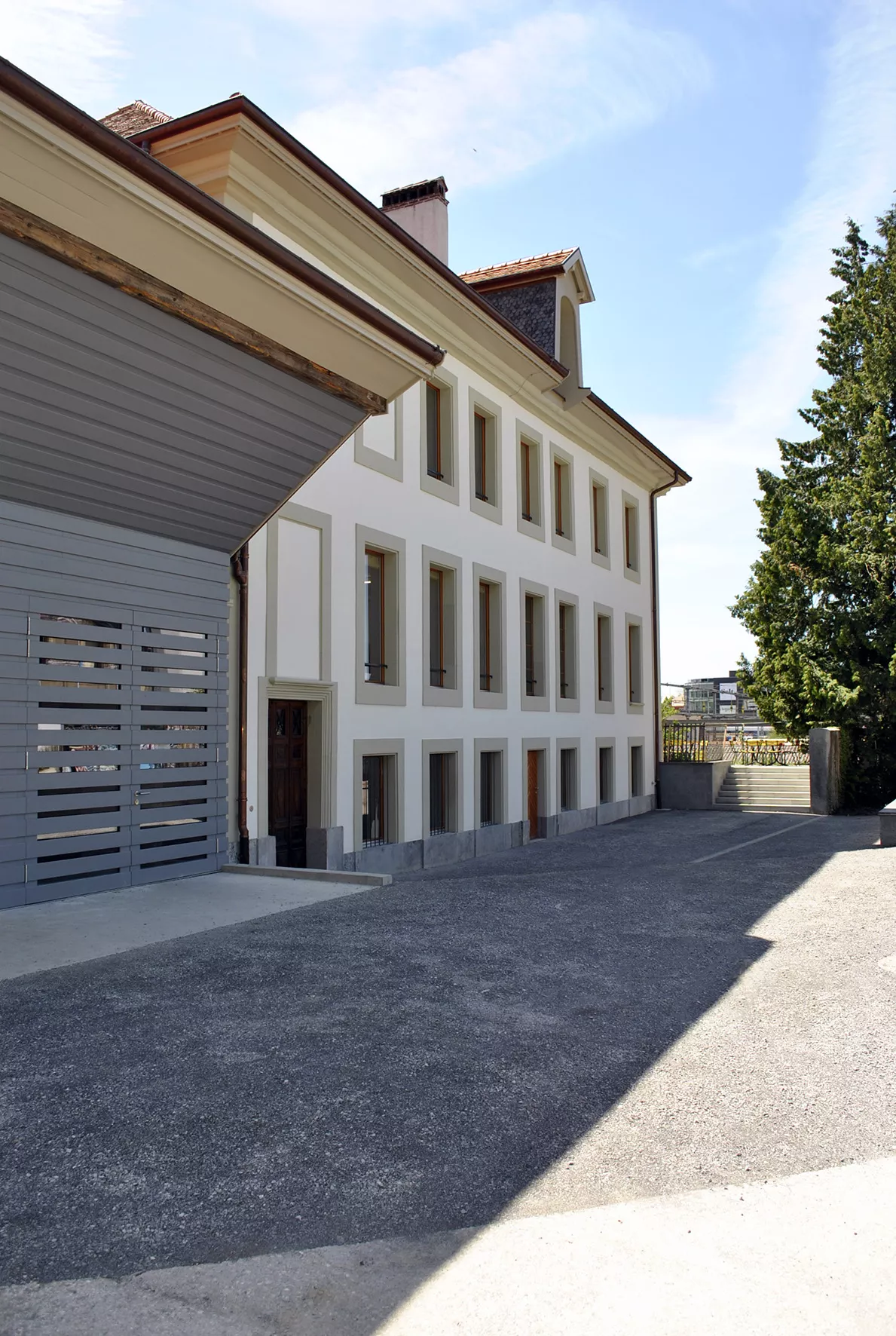 Bâtiment annexe de la Ferme des Tilleuls, crépi blanc et bardage gris le long de la cour