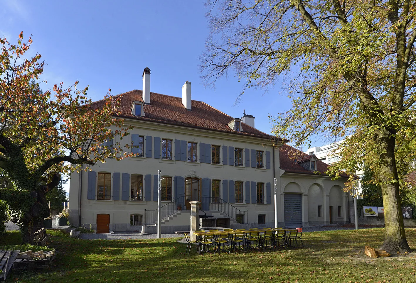 Ferme des Tilleuls en automne, façade à volets bleus derrière les arbres