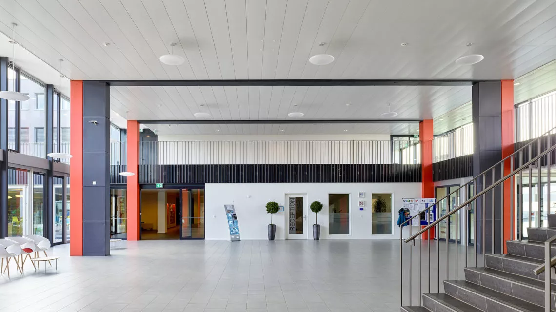 Hall d'entrée vitré de l'International School of Lausanne, piliers rouges et bleus et escalier