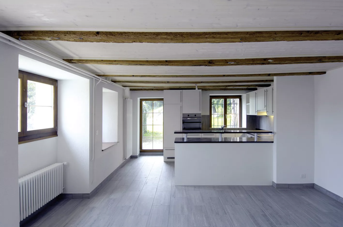 Pièce à vivre de la Ferme Creux avant emménagement, poutres apparentes et cuisine ouverte au fond