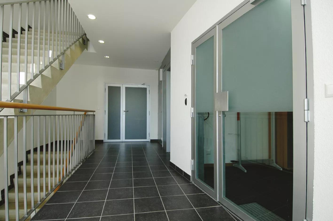 Palier carrelé de la résidence Sablons A avec porte vitrée et escalier