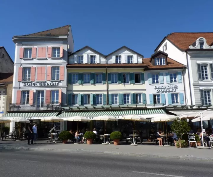 Façade de l'Hôtel du Port et de la Crêperie d'Ouchy sur le quai, volets colorés et terrasses sous stores rayés