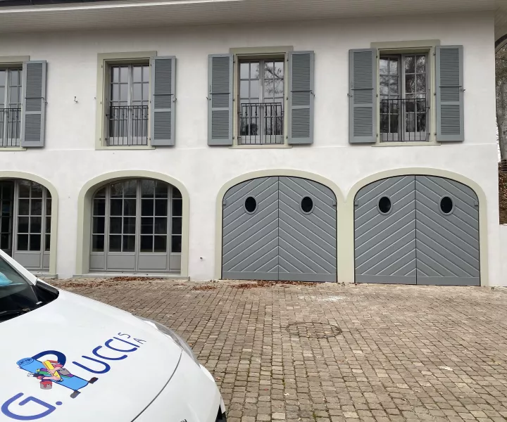 Façade de la maison de maître à volets gris et portes de garage cintrées, avec le véhicule G. Pucci SA